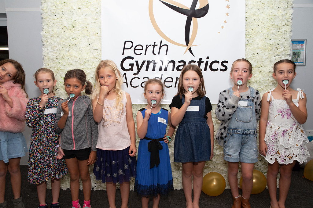 Several children eating lollipops in front of a sign that says Perth Gymnastics Academy